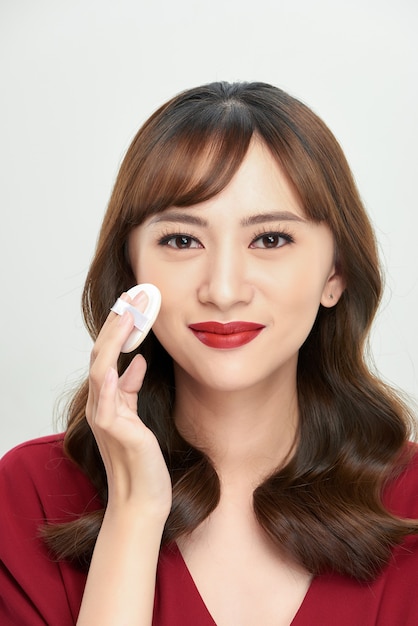Maquillaje belleza mujer asiática aplicando base en polvo en la cara.