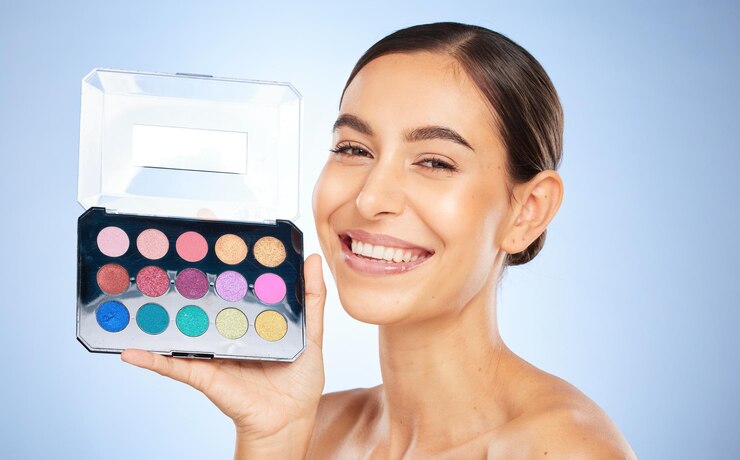 Foto maquillaje de belleza y paleta de sombras de ojos con una mujer modelo en estudio sobre un fondo azul para aplicar color cara de retrato y cosméticos con una atractiva mujer joven posando para promocionar un producto para la piel