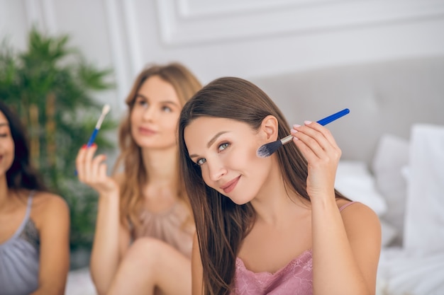 Maquillaje. Chica sonriente de pelo oscuro sosteniendo un pincel y haciendo maquillaje