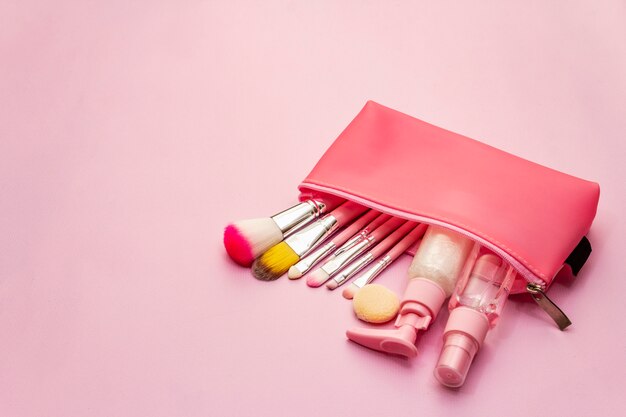 Maquillaje cosmético en bolsa sobre fondo rosa