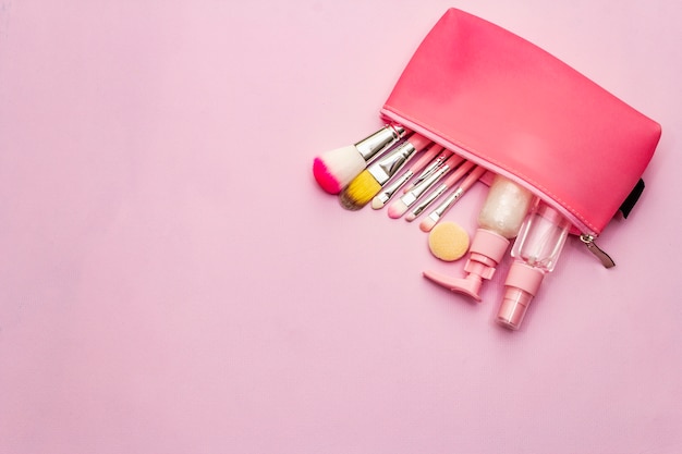 Maquillaje cosmético en bolsa sobre fondo rosa