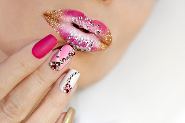 Maquillaje de labios rosa y blanco y manicura con pedrería