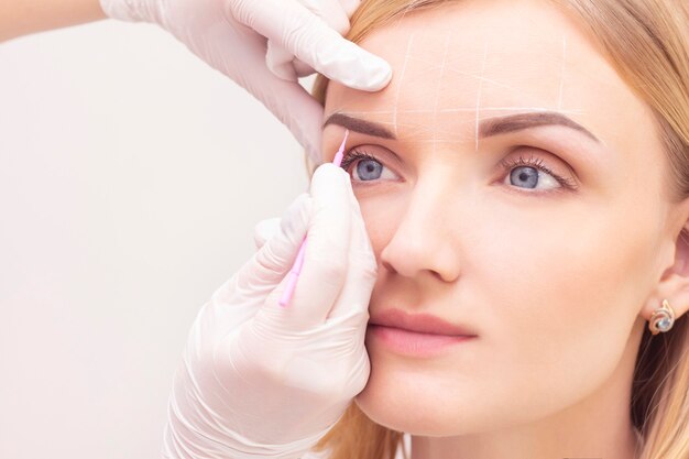 Maquillaje. Manos de esteticista haciendo tatuaje de cejas en el rostro de la mujer. Maquillaje permanente de cejas en el salón de belleza.