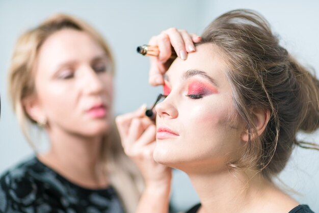 Maquillaje Maquillador aplica rímel a una chica con maquillaje brillante