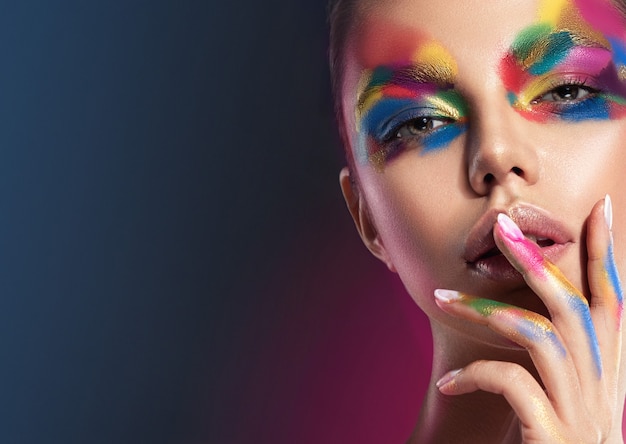 Maquillaje multicolor extravagante brillante en la cara de mujer joven y bonita Maquillaje y cosméticos