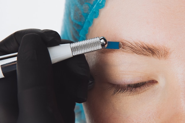 Maquillaje permanente para cejas. Ceja microblading. Esteticista haciendo tatuajes de cejas para rostro femenino. Hermosa joven en un salón de belleza