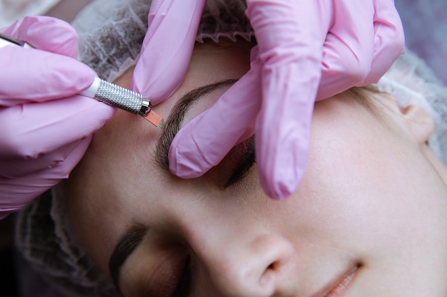 Foto maquillaje permanente para cejas. ceja microblading. esteticista haciendo tatuajes de cejas para rostro femenino. hermosa joven en un salón de belleza