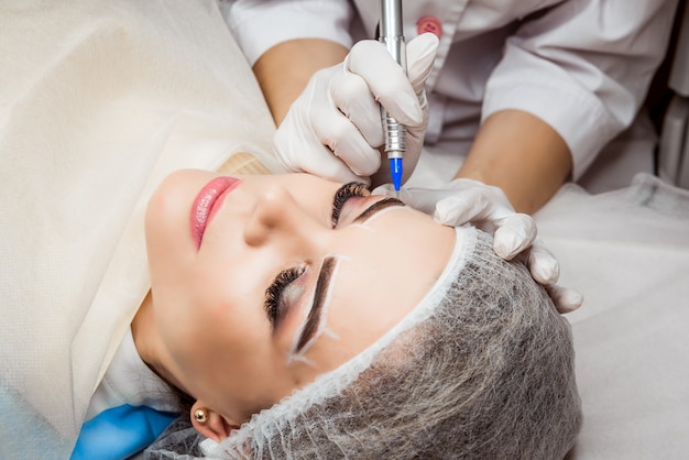 Maquillaje permanente para cejas. Primer de la mujer hermosa con las cejas gruesas en salón de belleza. Esteticista haciendo tatuajes de cejas para rostro femenino. Procedimiento de belleza