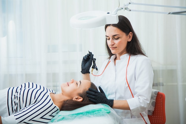 Maquillaje permanente para cejas en salón de belleza. Esteticista tatuando las cejas de una mujer joven. Corrección de cejas.