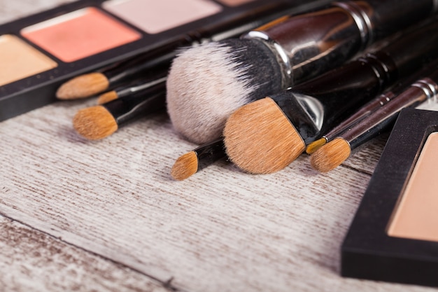 Maquillaje pinceles y productos cosméticos en foto de cerca en mesa de madera