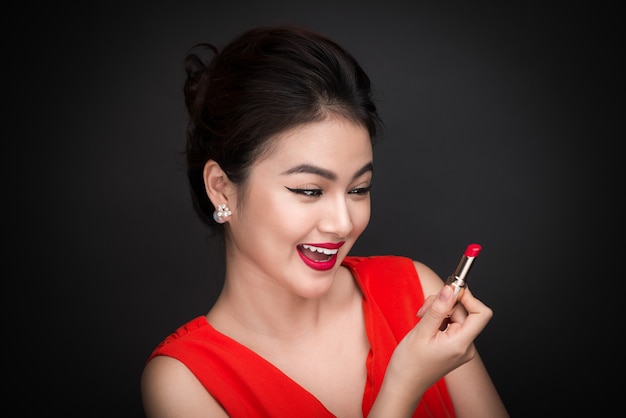 Maquillaje profesional. Modelo asiático atractivo que aplica el lápiz labial rojo.