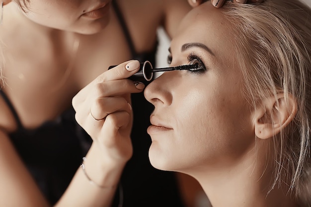 maquillaje profesional en el salón de belleza / maestro hace un maquillaje profesional de verano fresco de una hermosa modelo en el salón