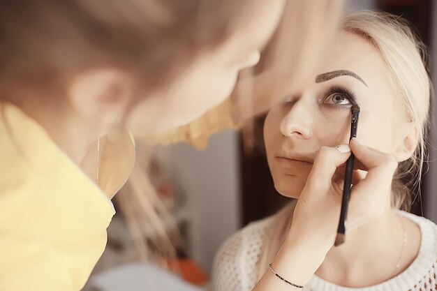 maquillaje profesional en el salón de belleza / maestro hace un maquillaje profesional de verano fresco de una hermosa modelo en el salón