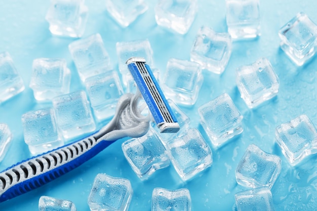 Máquina de afeitar azul con cuchillas afiladas en el fondo del primer plano de cubitos de hielo