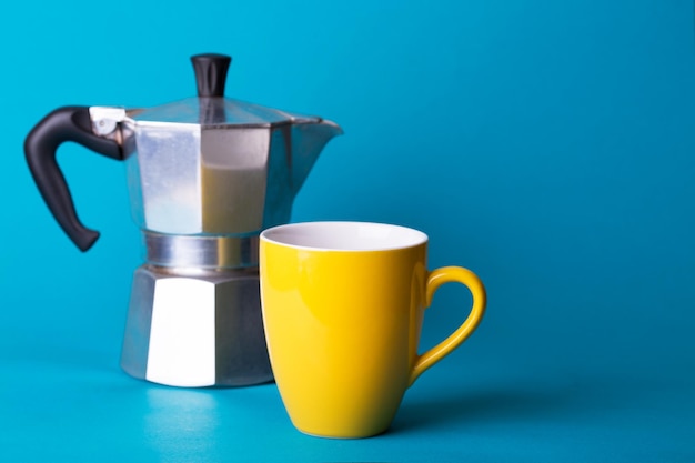 Máquina de café géiser y una taza amarilla sobre un fondo azul.