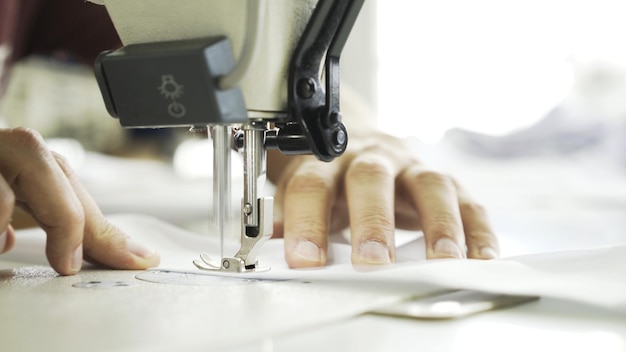 Máquina de coser cerca de manos y tela blanca