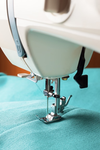 Máquina de coser con hilo y tela turquesa, primer plano