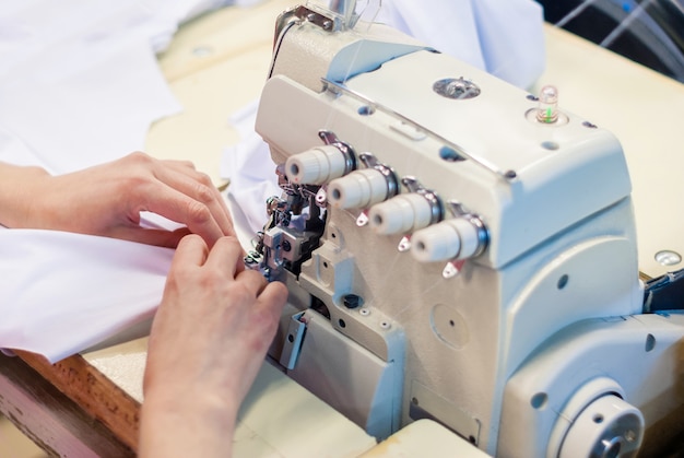 Máquina de coser overlock industrial y manos de costurera en el trabajo en la fábrica de ropa