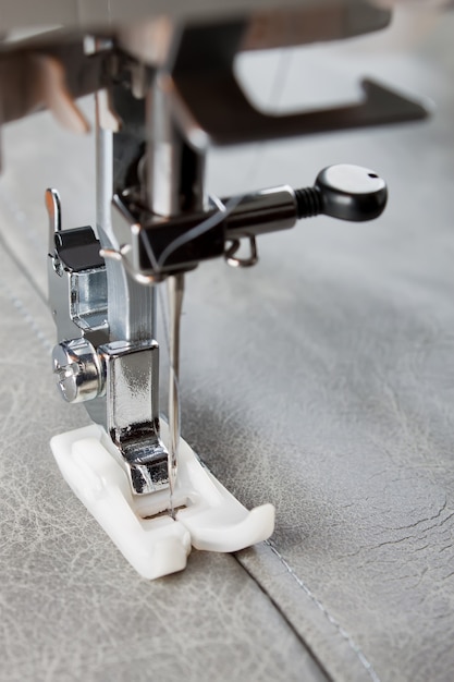 La máquina de coser con prensatelas especial realiza una costura sobre cuero gris. proceso de costura de cerca