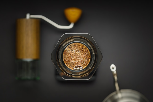 Máquina de café Aeropress com escalas, moedor de café e chaleira em uma vista superior da superfície preta.