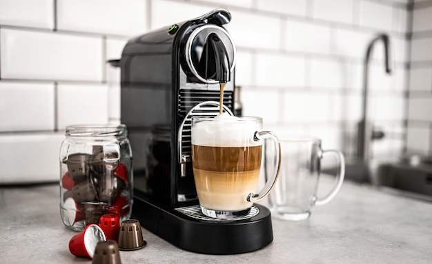 Máquina de café com cápsulas e cappuccino cremoso em copo transparente em casa café espresso beve