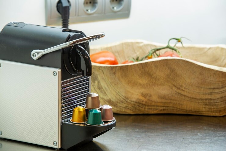 Foto máquina de café de cápsula em uma fruteira preta com tomates e cápsulas de vários tipos
