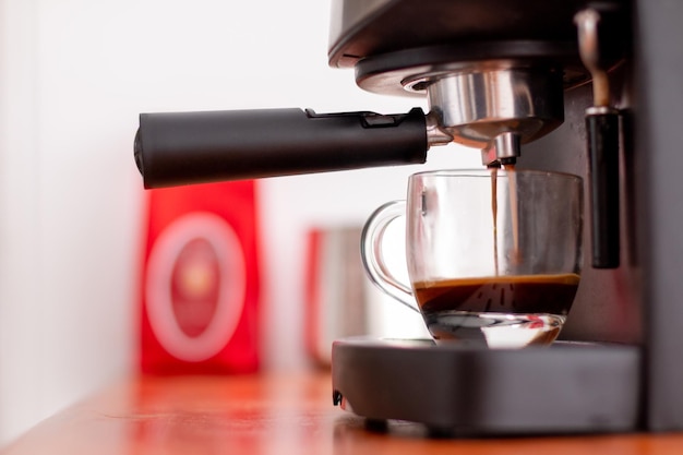 Máquina de café instantâneo preparando café em um copo transparente meio cheio.