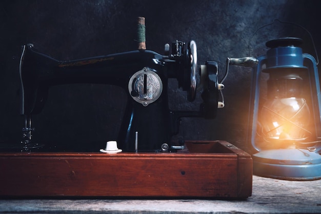 Máquina de costura velha, retrô, vintage e uma lâmpada de querosene em um fundo escuro de uma parede abstrata.