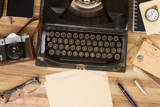 Máquina de escrever antiga preta com suprimentos na mesa de madeira, copie o espaço em papel envelhecido