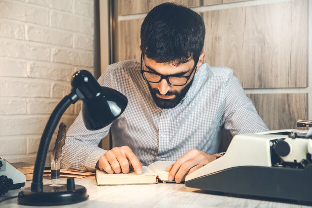 Máquina de escrever e homem lendo livro na mesa