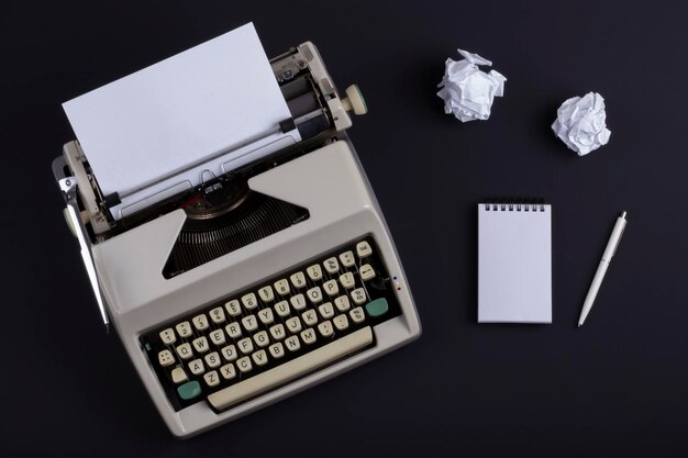 Foto máquina de escrever velha com uma folha de papel em branco perto de uma caneta de bloco de notas e papel amassado