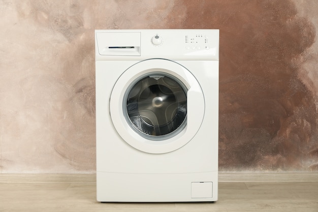 Foto máquina de lavar roupa moderna contra parede marrom, espaço para texto