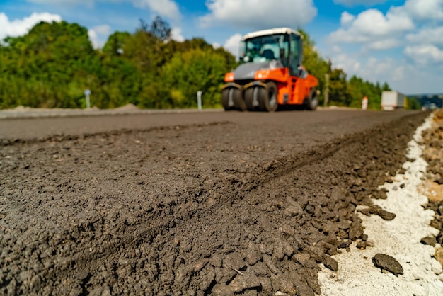 Máquina de pavimentação industrial colocando asfalto fresco no canteiro de obras da rodovia. Veja de baixo em técnica especial. Foco seletivo.