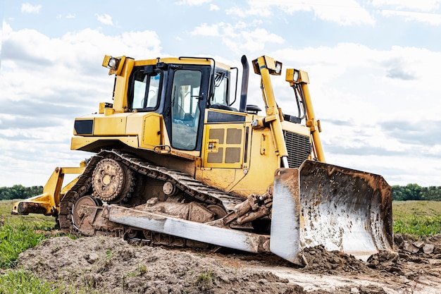 Máquina escavadora está nivelando o canteiro de obras. O Earthmover com a lagarta está movendo a terra. Fechar-se. Maquinaria pesada de construção.