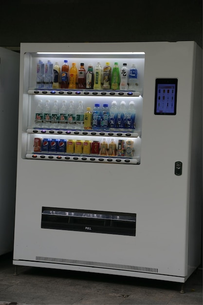 Máquina expendedora blanca en vista frontal a color con una pantalla de visualización en el lado superior derecho y botellas de refrescos en el interior