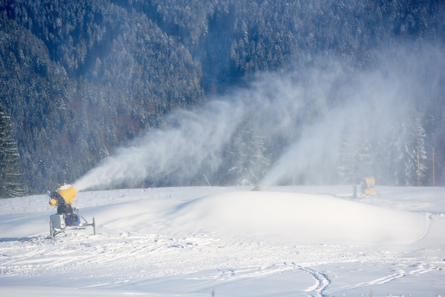 Máquina de fabricación de nieve eléctrica rociando nieve artificial en la ladera de la montaña. Preparación para la apertura de una nueva temporada de esquí.