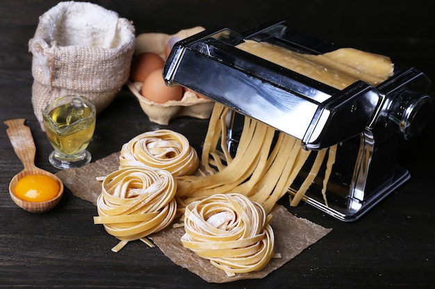 Máquina para hacer pasta de metal e ingredientes para pasta en mesa de madera