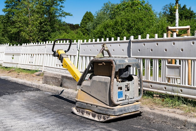 Máquina manual de tampagem de estradas em um canteiro de obras em frente a uma cerca branca de plástico
