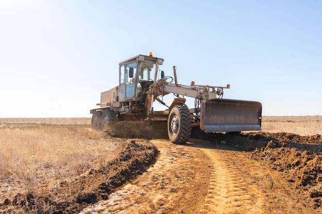 Una máquina niveladora que hace una nueva carretera, excava la tierra de grava en el campo