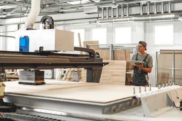 Foto máquina de operación de carpintero joven para procesamiento de madera en una fábrica de muebles de cerca