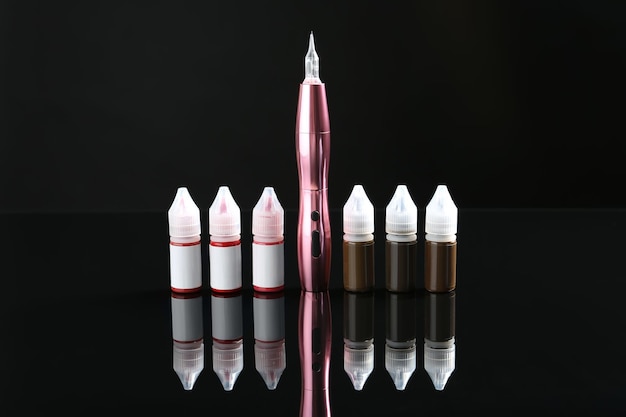 Máquina profesional de maquillaje permanente y botellas de pigmentos en superficie de espejo negro