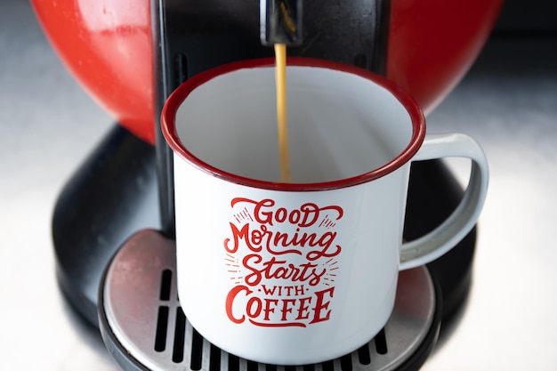 Máquina que prepara una cápsula de café con una taza con inscripciones