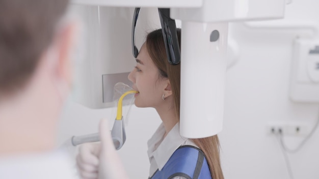 En una máquina de rayos X panorámicos, el dentista alinea la mordida de una mujer En una clínica dental, una mujer vestida con un delantal de plomo permanece inmóvil mientras una máquina de rayos X panorámicos gira alrededor de su cabezaxA