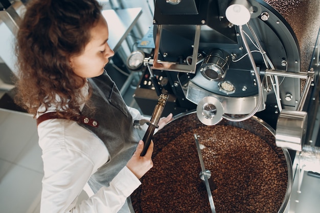 Máquina tostadora de café y barista con tryer en el proceso de tostado de café.