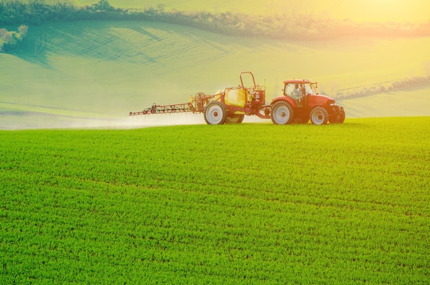 Maquinaria agrícola rociando insecticida al fondo de primavera estacional natural agrícola de campo verde