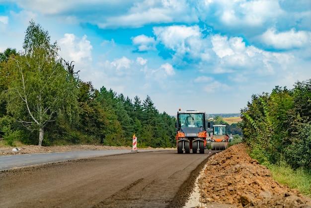 La maquinaria de construcción para obras viales pasa a través del nuevo asfalto en el verano de los árboles.