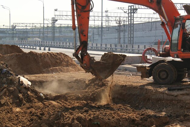Máquinas de escavadeira trabalhando no canteiro de obras da nova estrada para a cidade. A retroescavadeira alaranjada escava a areia a