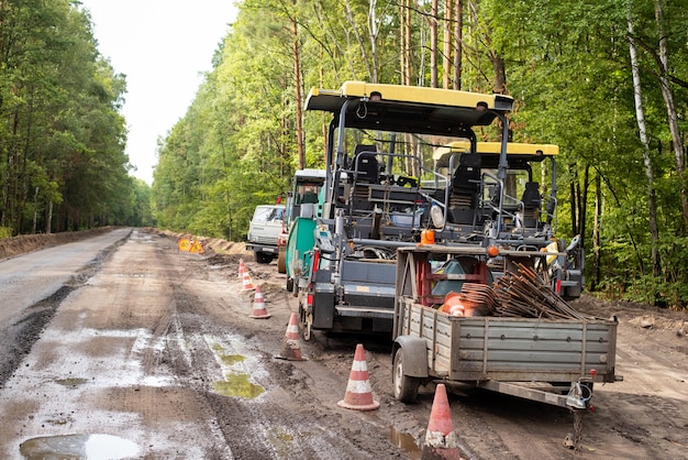 Máquinas modernas para a construção de estradas de asfalto na estrada lateral. Pausa na construção de novas estradas devido ao mau tempo chuvoso