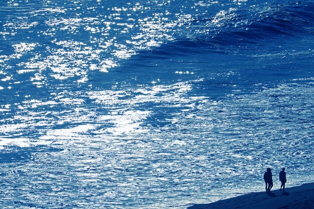 Mar azul ondulado con la silueta de un grupo de personas caminando por la playa