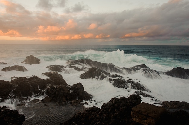 Mar azul tempestuoso e muitas pedras sob o céu nublado durante o pôr do sol na noite de verão